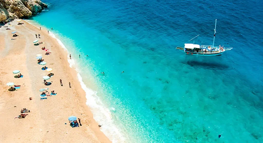 Kaputaj Plajında insanlar denize giriyor ve bir tur teknesi demirlemiş