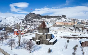 Kars Kalesi ve Kümbet Camiinin kışın karla kaplı, gri taş mimarisi ve kırmızı çatısı.